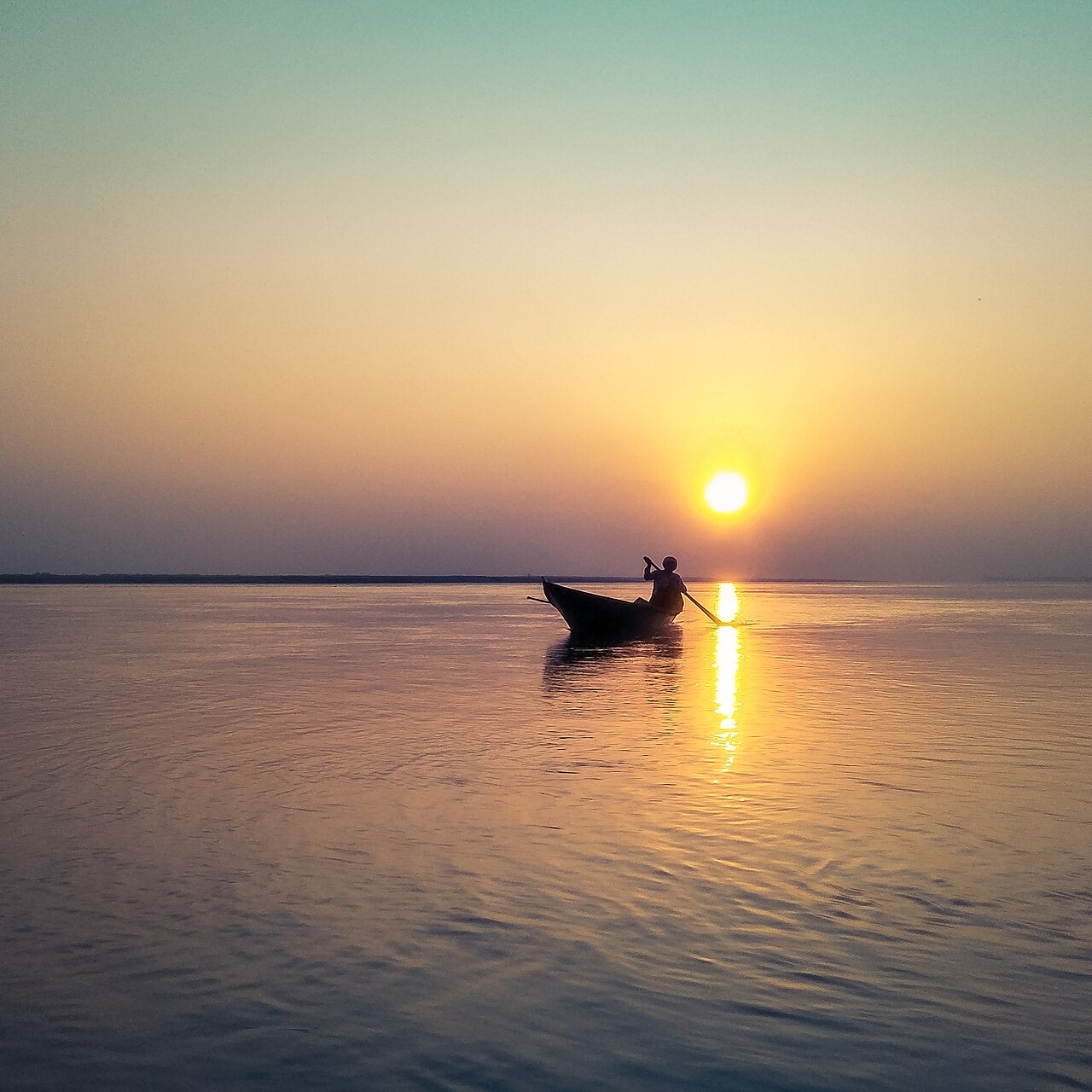 A lone fisherman rowing a small boat on the Brahmaputra river at sunset